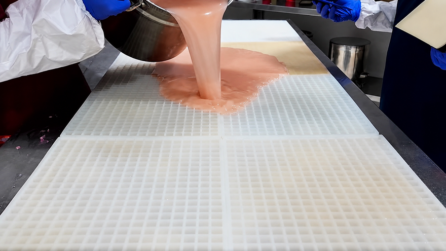 Equipo de Gummy Molds vertiendo mezcla de gomitas sobre un molde comercial grande de silicona antes de raspar